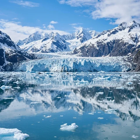 Alaskan glacier and snowy mountains reflected in calm water