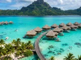 Overwater bungalows in a South Pacific lagoon below a green peak
